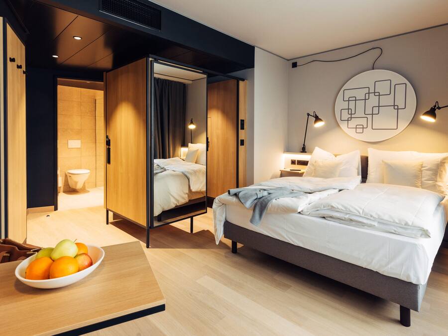 Una habitación de hotel moderna con una cama grande, mesitas de noche, un frutero y una obra de arte original en la pared.