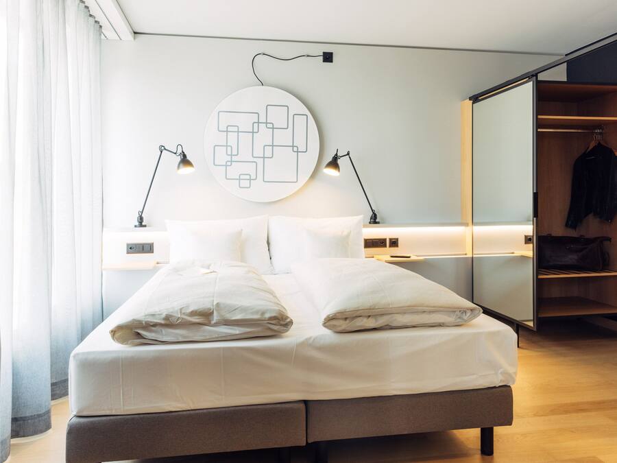 Un dormitorio moderno con cama, lámparas de noche, una obra de arte en la pared y un armario.
