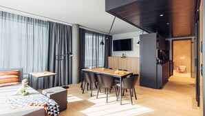 Une chambre d’hôtel moderne dotée d’un coin repas, d’un canapé, d’une petite table avec une lampe et d’un téléviseur fixé au mur.