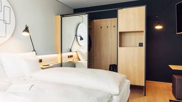 Una habitación de hotel moderna con una cama grande, un escritorio con lámpara, un armario y un espejo.
