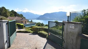 A paved pathway leading to a gated entrance with a view of a lake and mountains in the background. - Apartment in Verbania near Lake and Islands (Verbania)