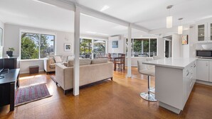 A spacious living area with a large sofa, dining table, and kitchen area with white cabinets and a large island.