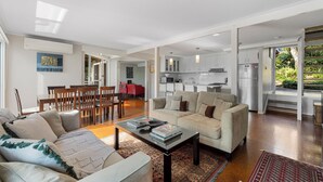 A spacious living area with a sofa set, a coffee table, and a dining table with chairs. There is a kitchen area with cabinets and appliances visible through an open doorway.