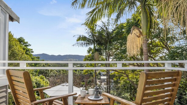 A wooden deck with two chairs and a table, overlooking a scenic landscape with trees and mountains.