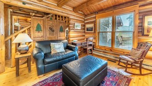 A log cabin interior with a leather sofa, a rocking chair, a dining table, and a large window with blinds. - 88 Potentilla Lane by Summit County Mountain Retreats (Keystone)