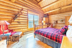 A log cabin bedroom with a bed, a bench, a table, and a window. - 88 Potentilla Lane by Summit County Mountain Retreats (Keystone)
