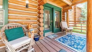 A log cabin with a porch, wicker chairs, a blue rug, and a wooden bench. - 88 Potentilla Lane by Summit County Mountain Retreats (Keystone)