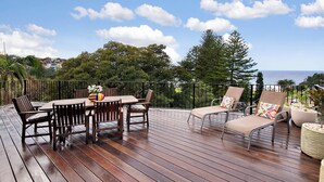 A wooden deck with a table and chairs, overlooking a scenic view of the ocean and trees. - Magnificent 3BR Bronte Holiday House with Views (Bronte)