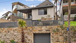 A modern two-story house with a stone facade, a grey garage door, and a balcony with a railing. - Magnificent 3BR Bronte Holiday House with Views (Bronte)
