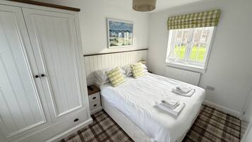 A bedroom with a large wardrobe, a bed with white linens, a checkered floor, a window with a view, and a painting on the wall.
