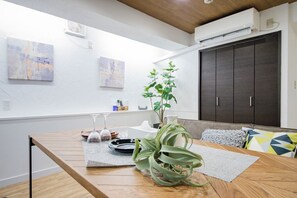 A dining area with a wooden table, two wine glasses, a potted plant, and a grey rug. There are two abstract paintings on the wall and a dark cabinet in the background. - THE HARMONY (Sapporo)