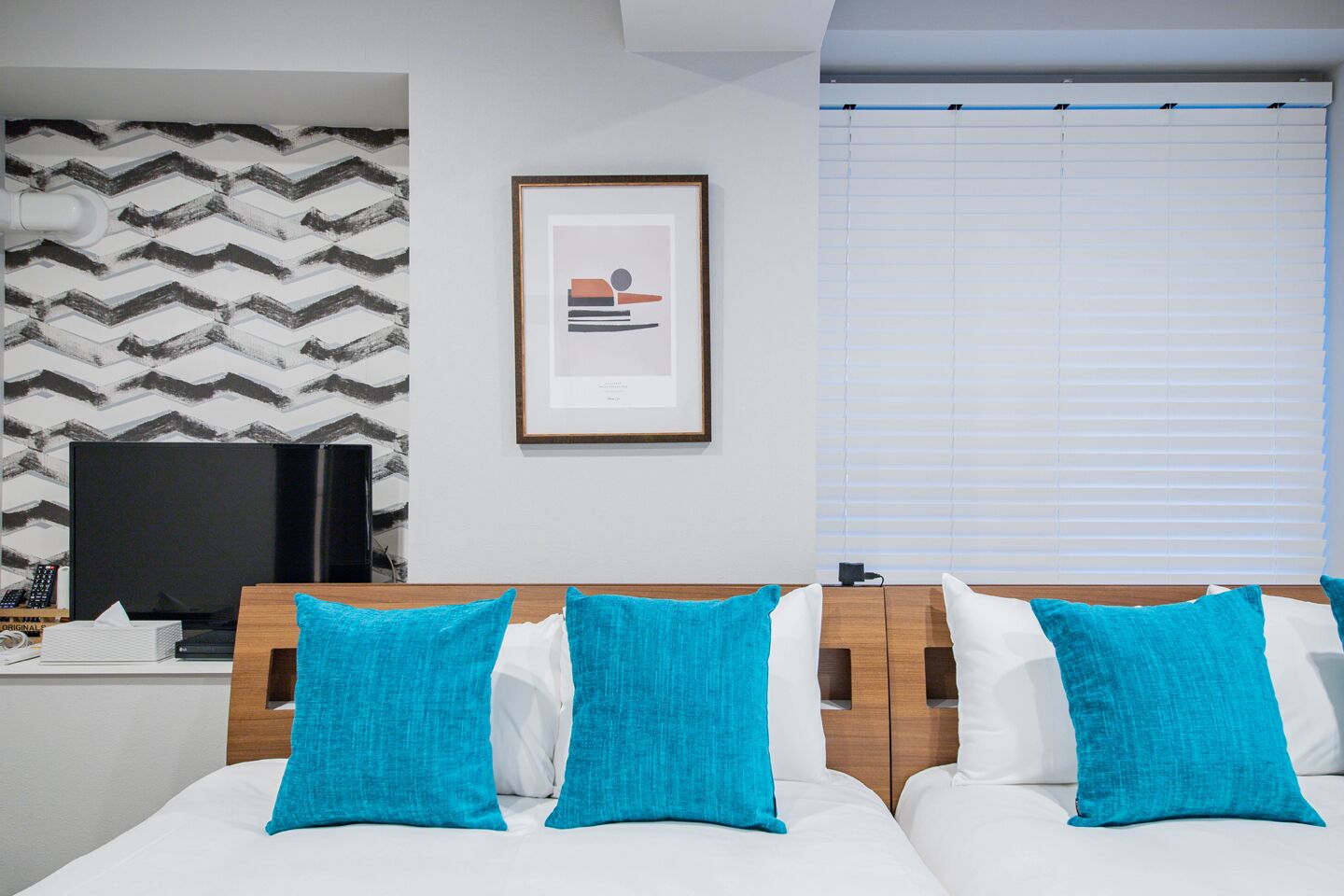 A hotel room with a modern design, featuring a large bed with white and turquoise bedding, a wooden headboard, a flat-screen TV, and a patterned wall.