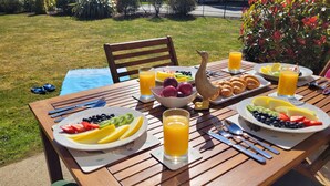 Een houten tafel gedekt met ontbijtbestek, fruit, croissants en glazen sinaasappelsap.