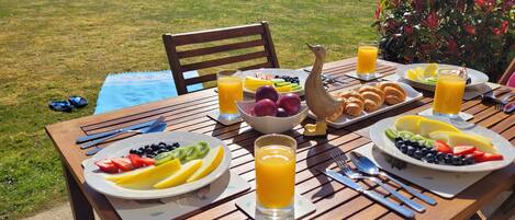 A wooden table set with breakfast plates, fruits, croissants, and glasses of orange juice.