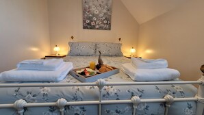 Een net opgemaakt bed met bloemenbedrukking, twee nachtkastjes met lampen, een dienblad met ontbijt, onder andere croissants, fruit en sap, en een schilderij aan de muur.