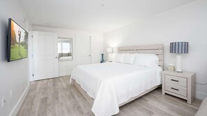 A bedroom with a bed, bedside tables, a TV, and a window. - Premier Ocean View Corner Condo (850S.F.) (Plymouth)