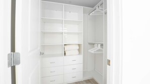 A walk-in closet with multiple shelves and drawers, a hanging rod, and a door with a silver handle. - Premier Ocean View Corner Condo (850S.F.) (Plymouth)