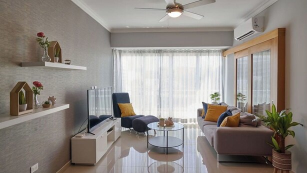 A modern living room with a ceiling fan, a flat-screen TV, a sofa, a coffee table, and decorative items on shelves.