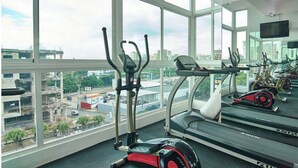 A gym with treadmills, elliptical machines, and stationary bikes, large windows offering a city view.