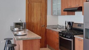 A modern kitchen with wooden cabinets, a granite countertop, a built-in oven, and a stainless steel refrigerator.