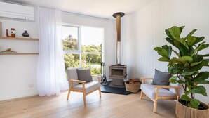Ein gemütliches Wohnzimmer mit Kamin, zwei Holzstühlen, einer großen Pflanze und Blick ins Grüne.