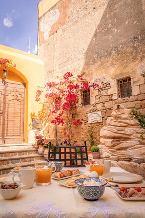 Una mesa servida con alimentos para el desayuno, una pared de piedra y una puerta de madera.