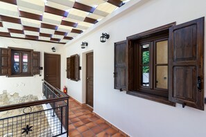 Stroll through this elegant corridor, lined with white walls and wooden doors, leading to a balcony with a scenic view.