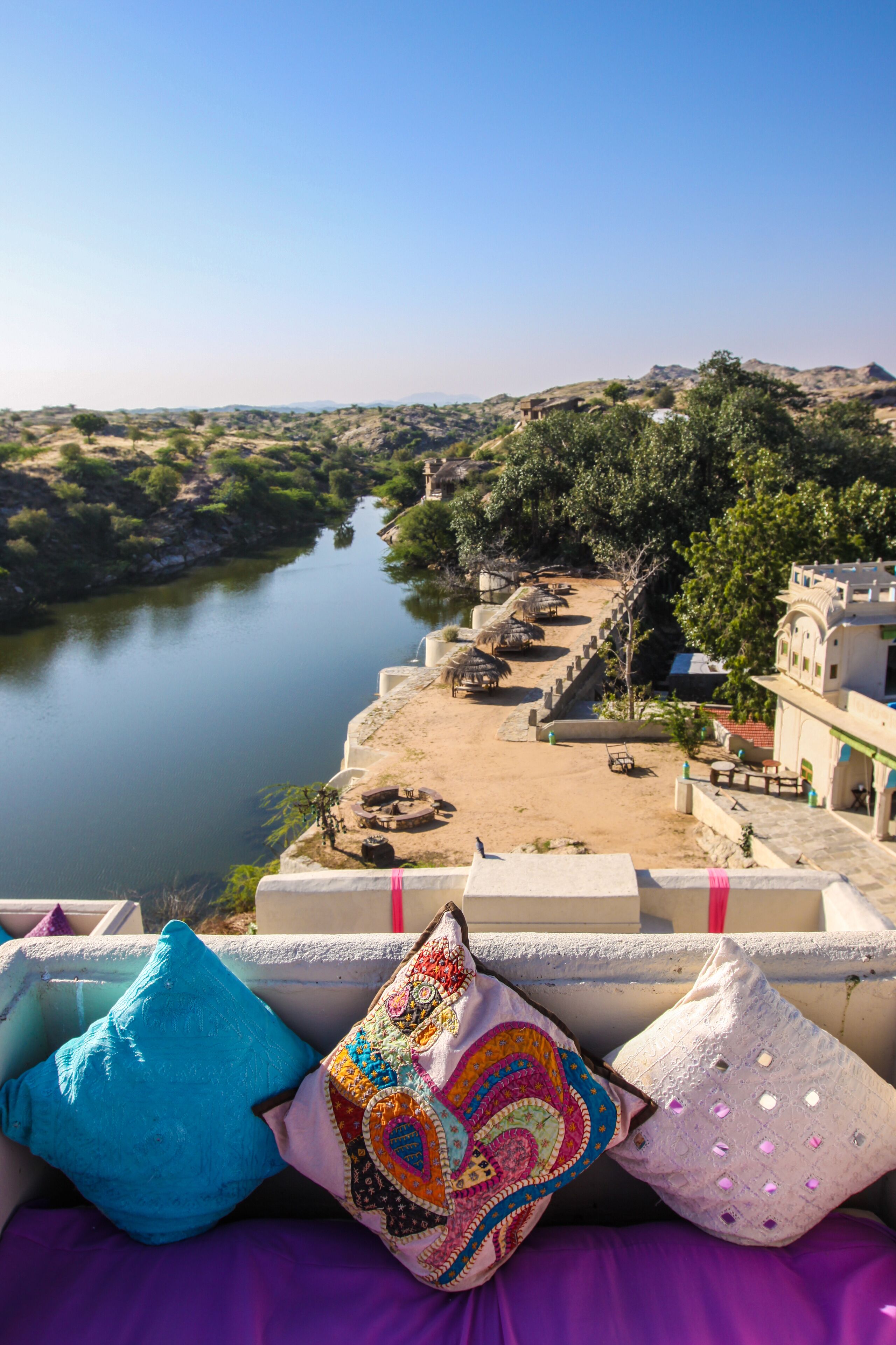 A balcony with colorful cushions overlooking a river and a traditional building.