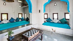 A room with two seating areas, each with a blue cushioned bench and a wooden table with a chessboard. - Brij Lakshman Sagar, Pali (Raipur)