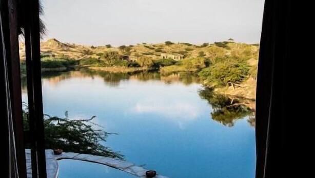 A view of a serene lake with a stone pathway leading to a seating area. - Brij Lakshman Sagar, Pali (Raipur)