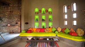 A cozy living room with a stone wall, a green sofa with colorful cushions, and a wooden coffee table. - Brij Lakshman Sagar, Pali (Raipur)