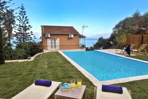 A swimming pool with lounge chairs and a table with drinks, surrounded by a well-maintained lawn and a house with a view of the sea. - Villa Litsa Large Private Pool Walk to Beach Sea Views A C Wifi (Corfu)