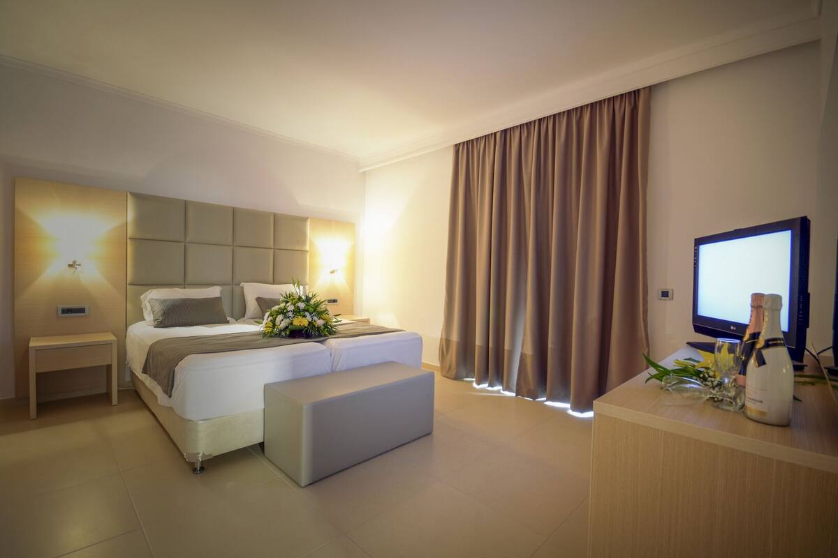 Una habitación de hotel moderna con una cama grande, mesitas de noche, un escritorio con computadora y una televisión.