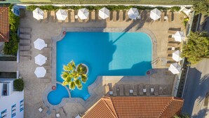 Vue aérienne d’un espace piscine avec des chaises longues et des parasols, entouré de bâtiments aux toits recouverts de tuiles.