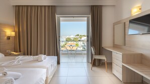 Une chambre d’hôtel avec deux lits, un bureau, une chaise, une télévision et un balcon offrant une vue sur les bâtiments et les arbres.