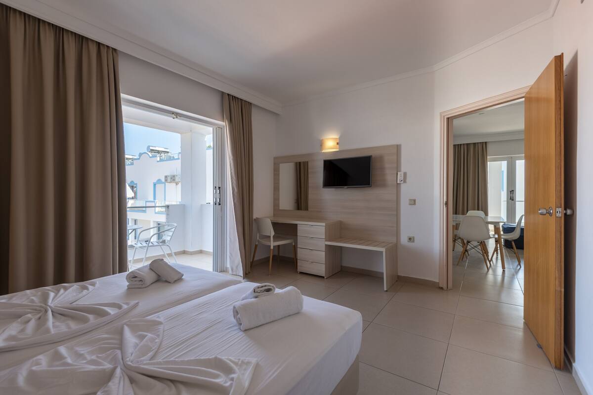 Una habitación de hotel con cama, escritorio, silla, televisor y balcón.