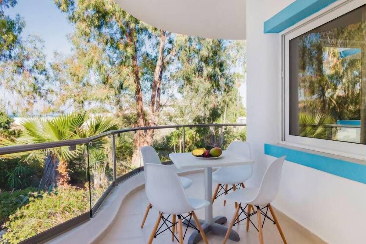 Un balcón con mesa y sillas, con vista a un jardín exuberante y árboles.