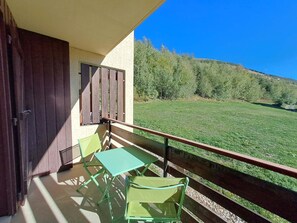 A balcony with a table and chairs, overlooking a grassy field and trees.