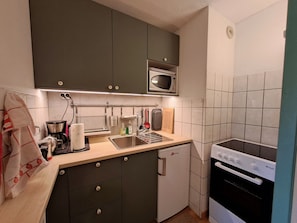 A compact kitchen with a microwave, stove, sink, and a small refrigerator.