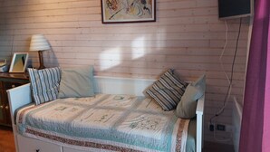 Ein Schlafzimmer mit einem Bett, einem Nachttisch, einer Lampe, einem gerahmten Bild an der Wand und einem an der Wand befestigten Fernseher.