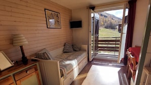 Ein gemütliches Zimmer mit einem Bett, einem Schreibtisch, einem Fernseher und einem Fenster mit Blick ins Freie.