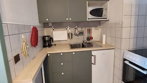 Eine kleine Küche mit grauen Schränken, einer Mikrowelle, einer Kaffeemaschine und einem Spülbecken.
