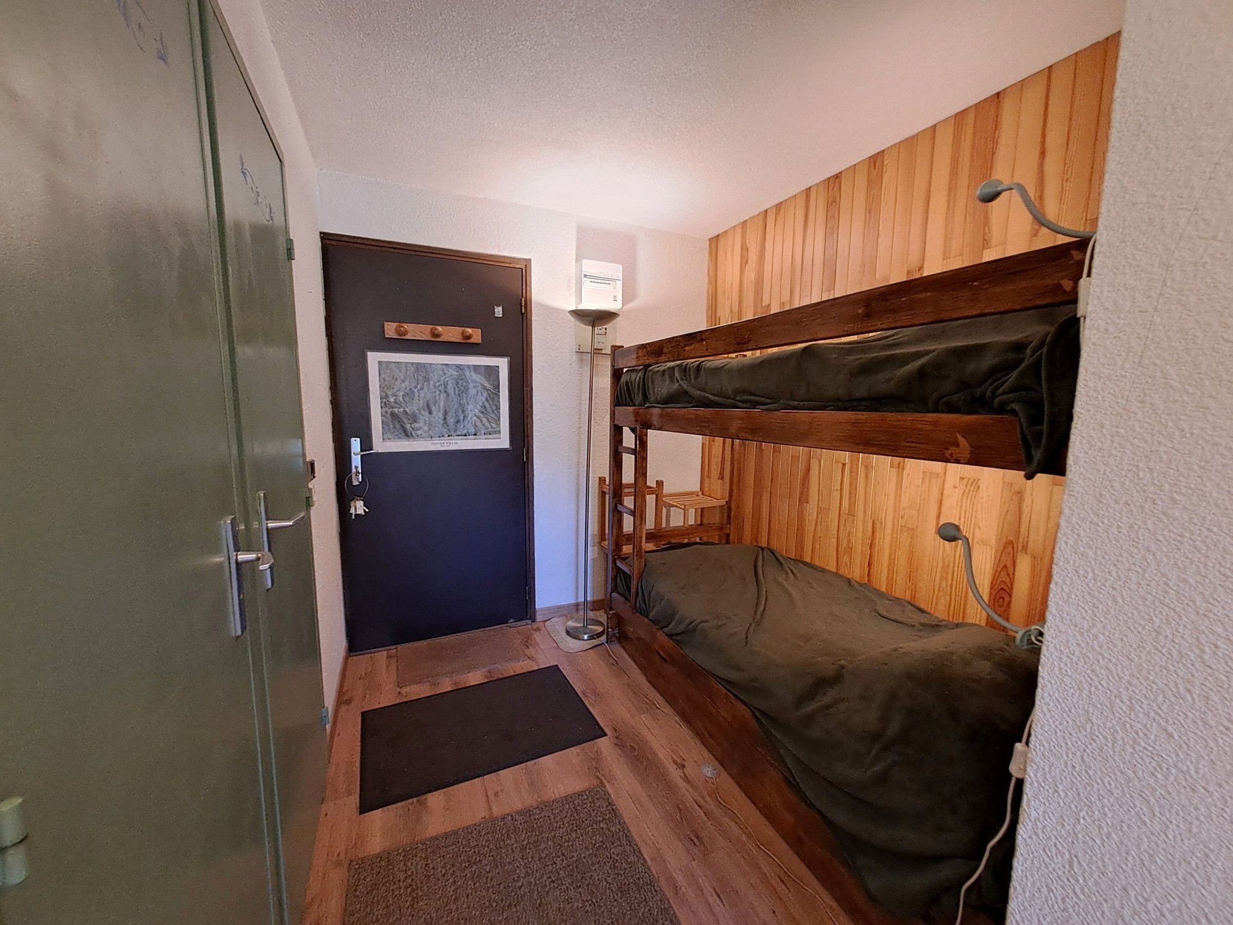 Ein kleines Zimmer mit Etagenbetten, einer Tür mit Schlüsselsperre, einer kleinen Matte und einer Wandleuchte.