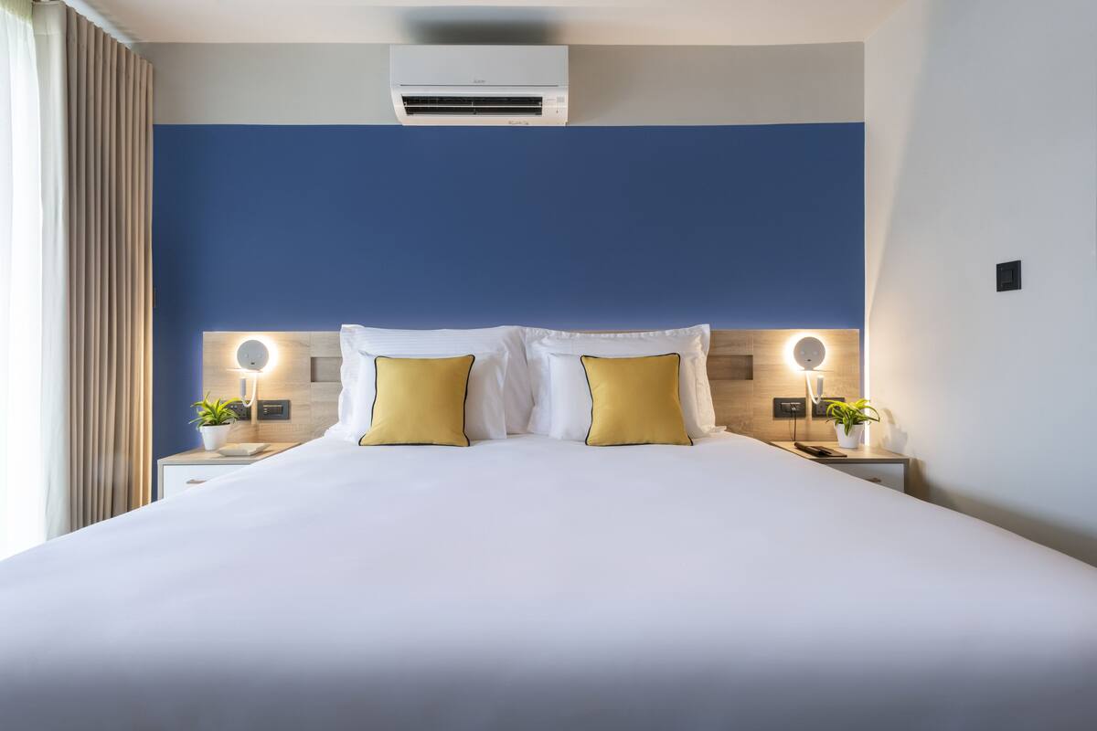 A hotel room with a large bed, two bedside tables with lamps, and an air conditioning unit above the bed.