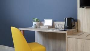 A modern room with a wooden desk, a yellow chair, a potted plant, a framed picture, a glass, and a black kettle. - Antoniel Suites (St. Julian's)