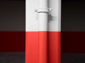 A close-up of a white pole with a red stripe, secured by a metal bracket.