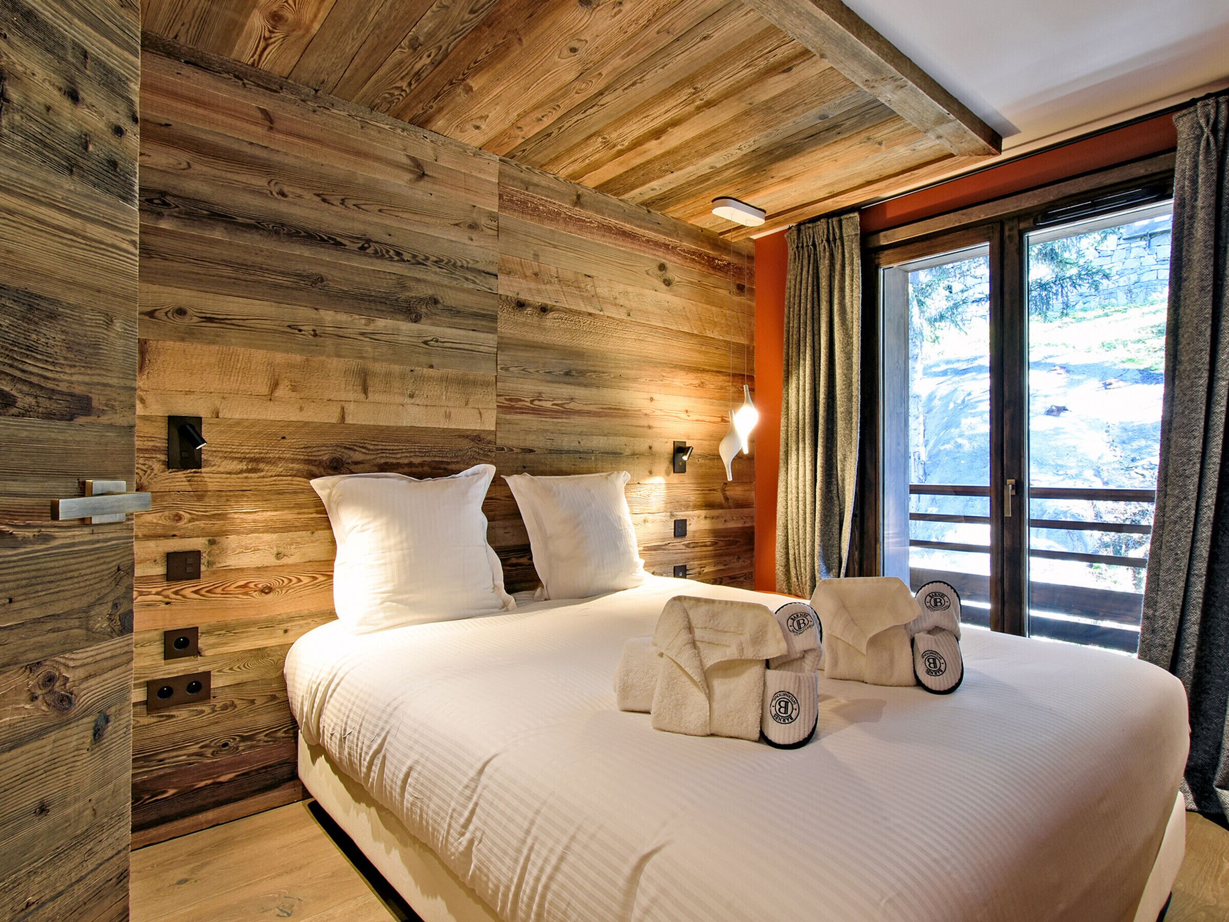 Ein Schlafzimmer mit Holzwandverkleidung, einem großen Bett, Kissen und Hausschuhen.