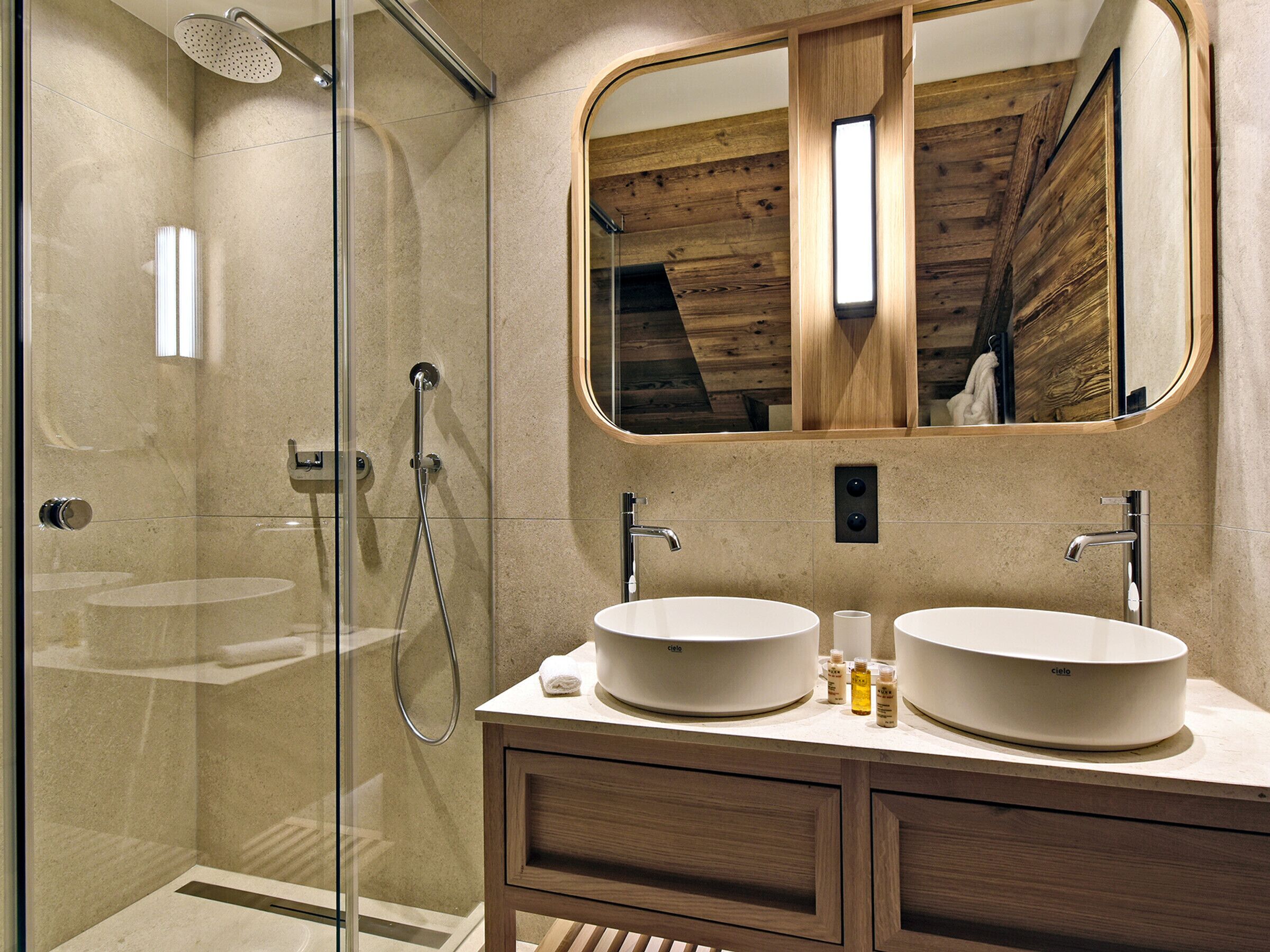 Une salle de bain moderne dotée d’une douche à parois de verre, de deux lavabos et d’un grand miroir.