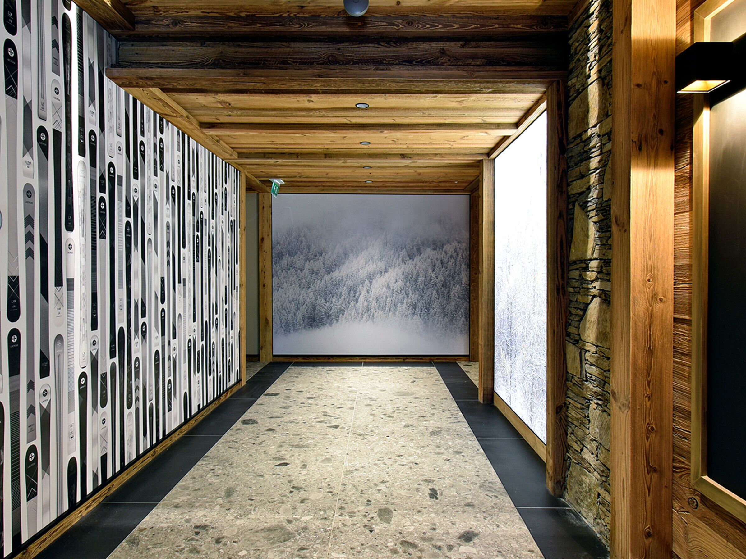A hallway with a wooden ceiling, a stone wall, and a large window with a snowy forest view.