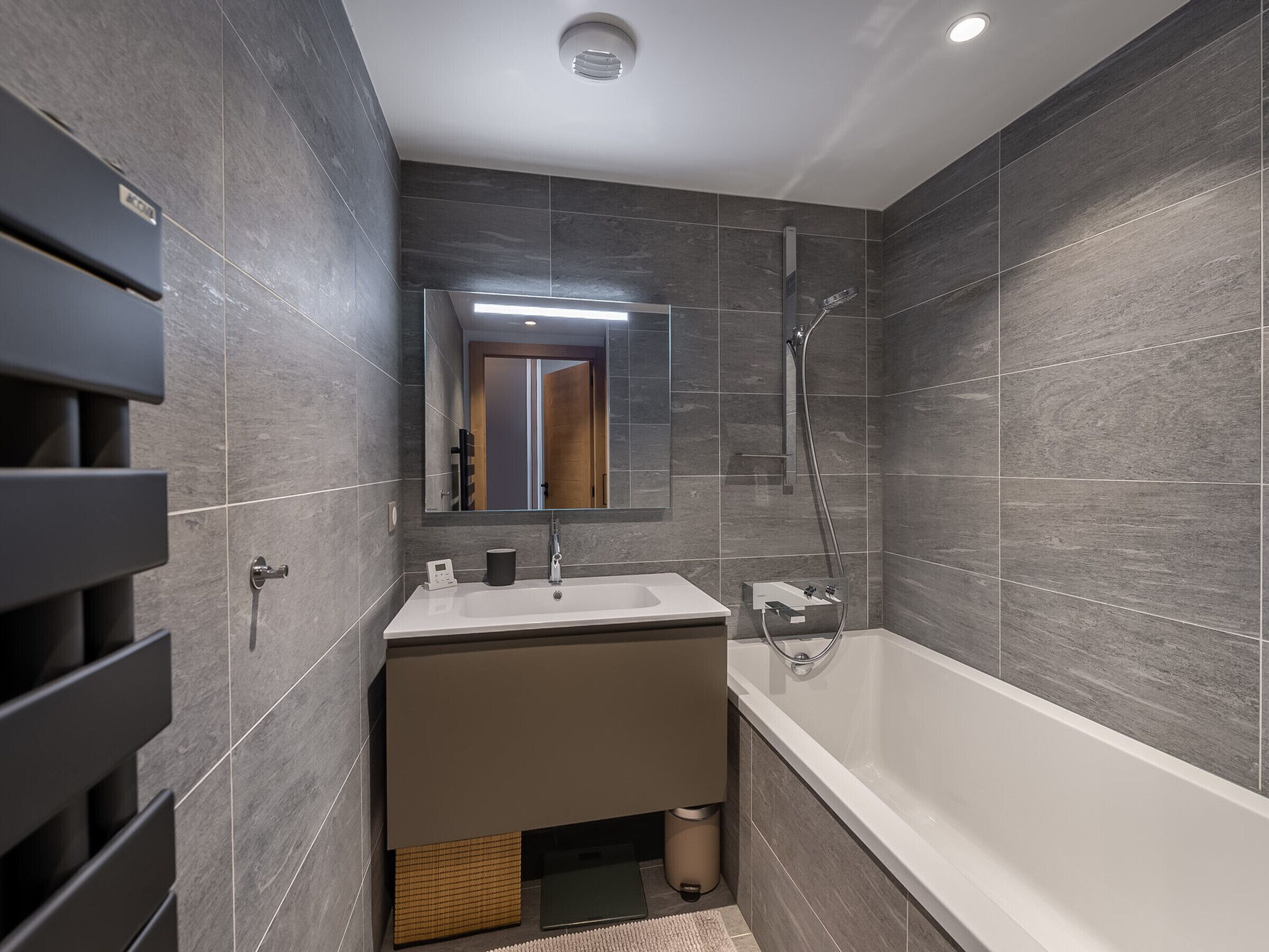 A modern bathroom with a large mirror, a bathtub, and a vanity with a sink.